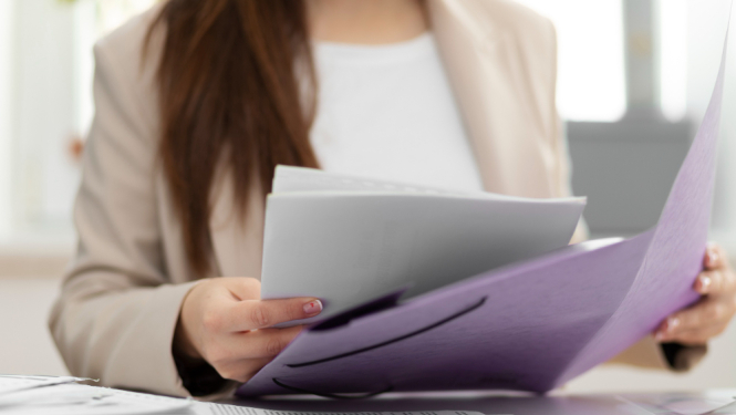 Sievietes rokas tur rokā dokumentu mapi