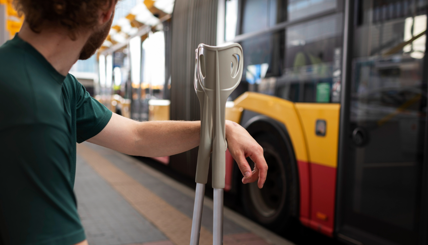 Sēž cilvēks ar kruķiem un fonā ir satiksmes autobuss
