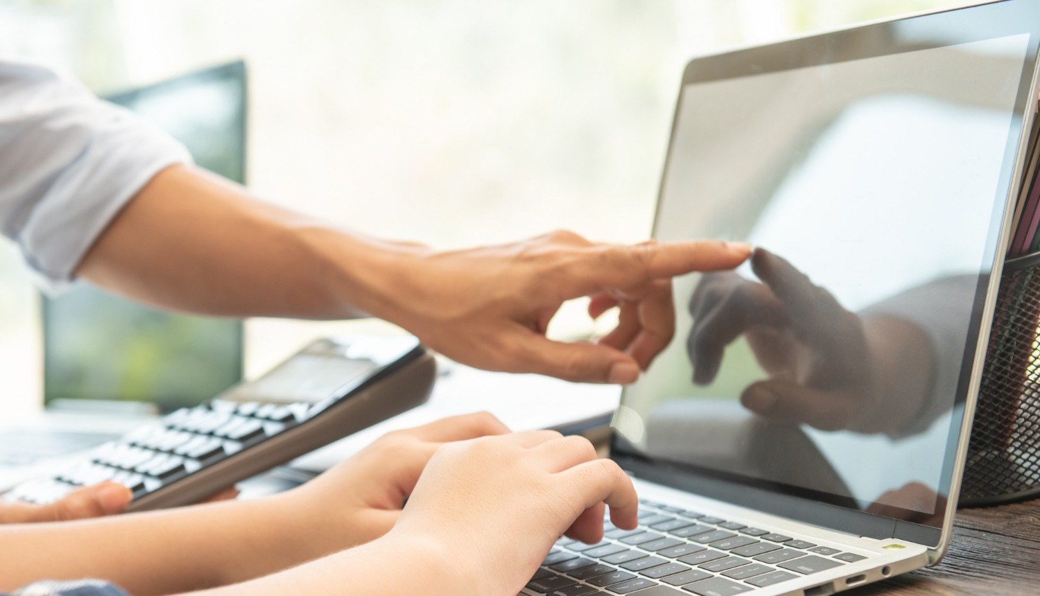 Cilvēka rokas uz klēpjdatora klaviatūras un rādītāja pirksts monitorā.